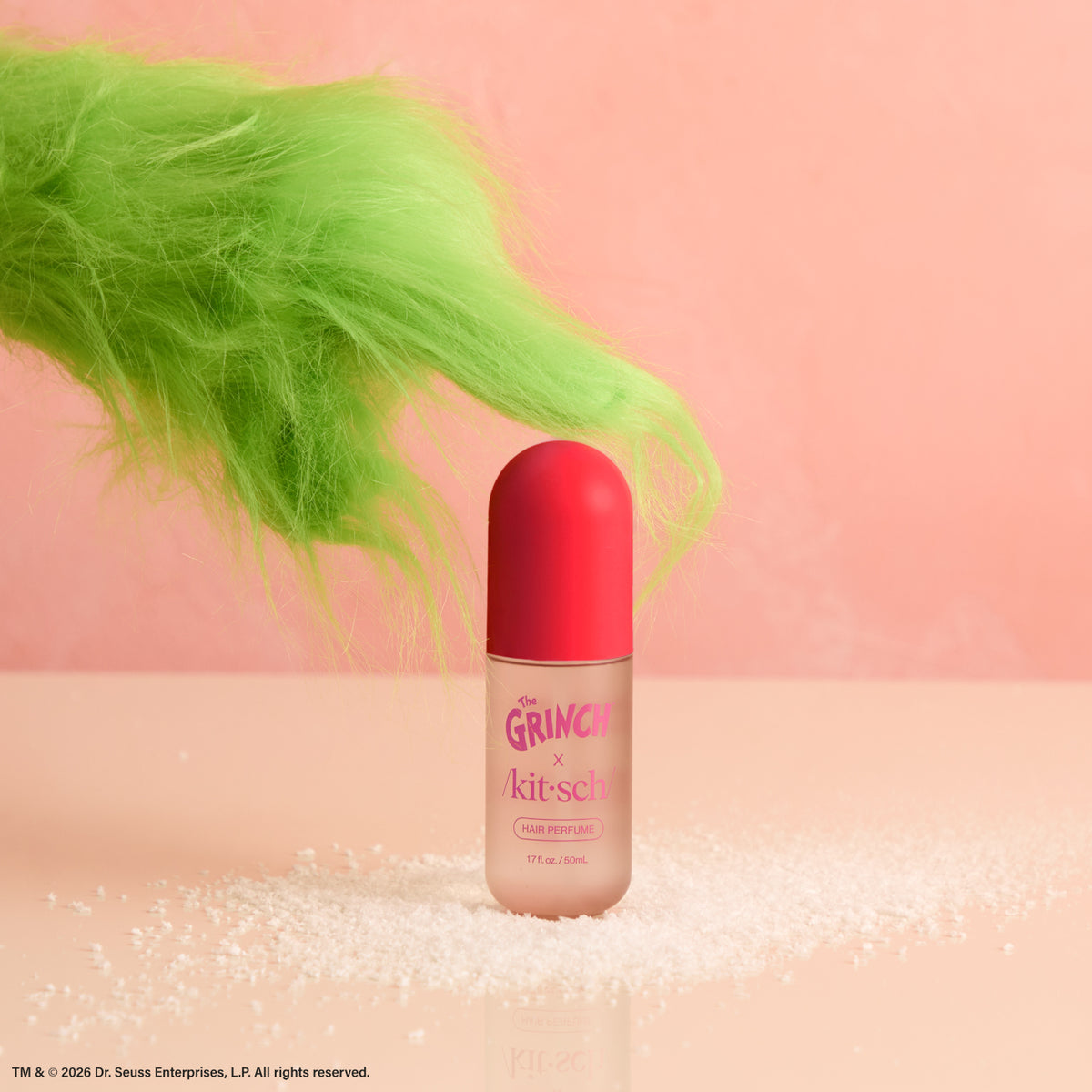 Green Grinch arm reaching for The Grinch x Kitsch Cherry Cheer Hair Perfume bottle