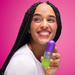 KITSCH Lisa Frank x Kitsch Cosmic Sundae Hair & Body Perfume Mist — smiling model with long braids holding the purple and green perfume mist bottle against a pink backdrop — eliminate bad smells, not just mask them, solo or layer — refresh your strands between washes