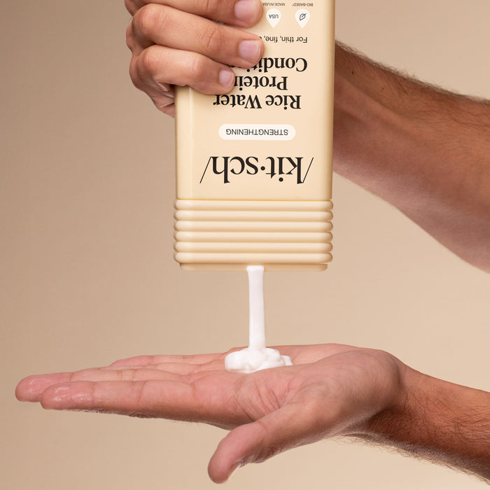 Hand holding a bottle of KitSch Conditoner with a visible pump, against a beige background.