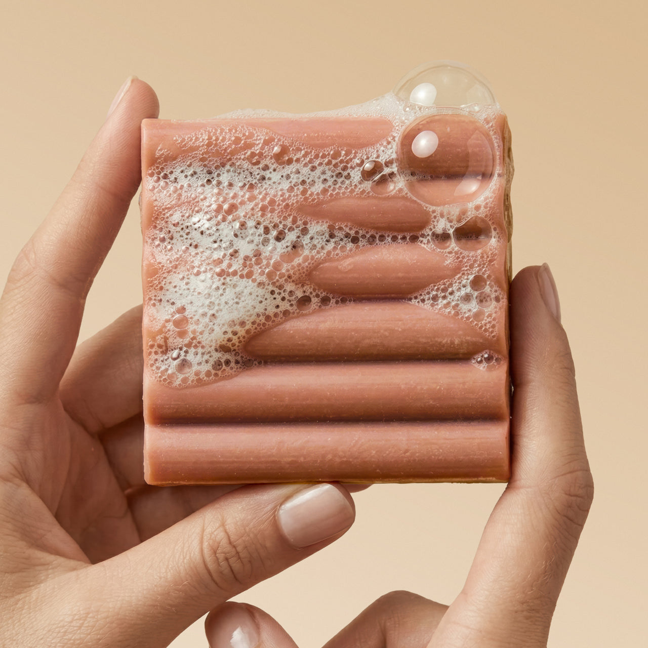 Close-up of hand holding Kitsch Amber Shores Body Wash Bar with rich sudsy lather and bubbles