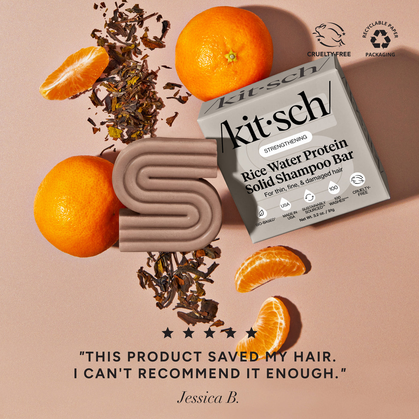 KITSCH Rice Water Shampoo Bar for Hair Growth — ingredient lifestyle flat lay on warm terracotta background — bar and retail box with mandarin oranges and dried tea leaves — Cruelty-Free | Recyclable Paper Packaging — 5-star customer review: "THIS PRODUCT SAVED MY HAIR. I CAN'T RECOMMEND IT ENOUGH." — Jessica B. — Formulated with Rice Tein NPNF® to increase hair volume by 20% after 5 washes